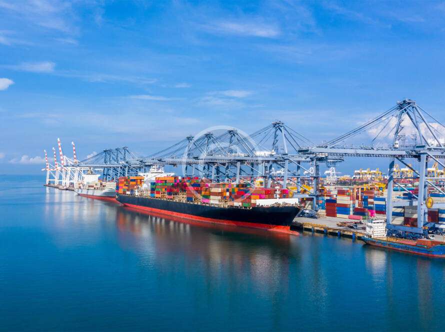 A cargo ship is docked at a busy port, surrounded by cranes and colorful shipping containers under a clear blue sky.
