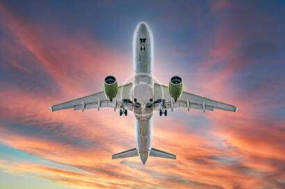 A large airplane viewed from below flies against a vibrant sunset sky.