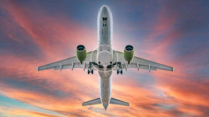 A large airplane viewed from below flies against a vibrant sunset sky.