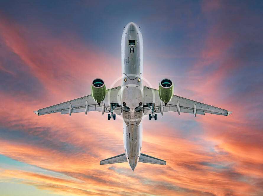 A large airplane viewed from below flies against a vibrant sunset sky.